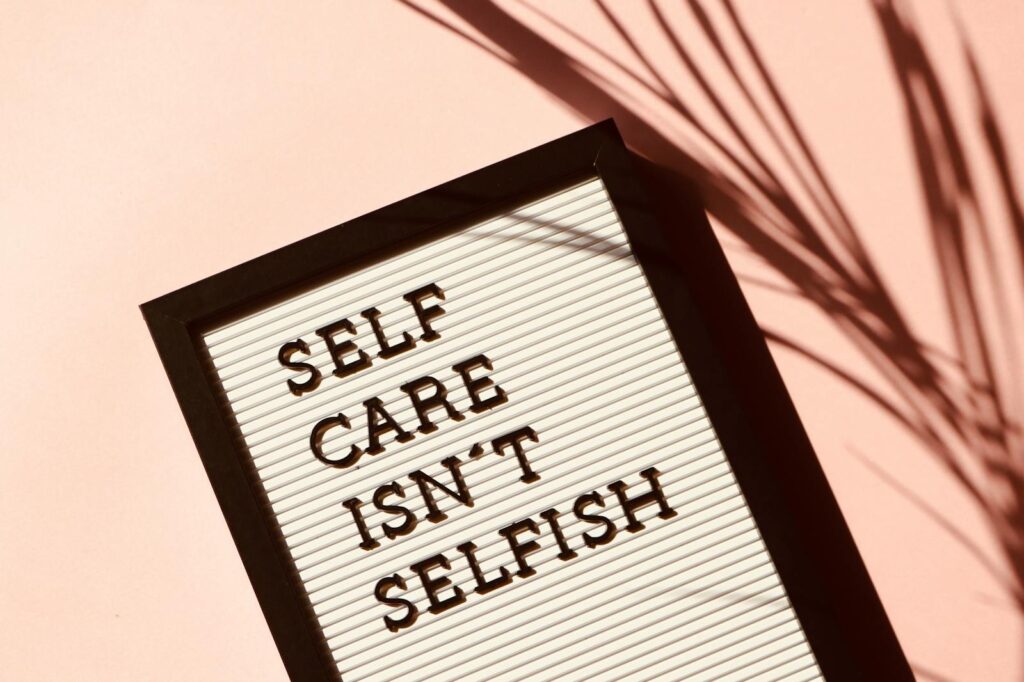 Letter board displaying 'Self Care Isn't Selfish' with artistic shadow on pink background.