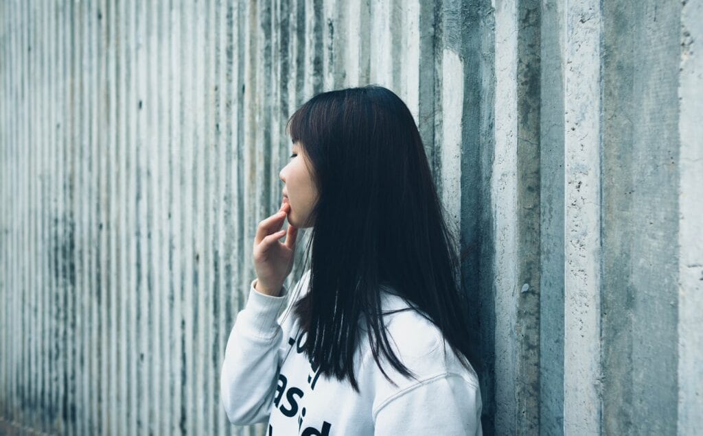 a woman leaning against a wall with her hand on her face