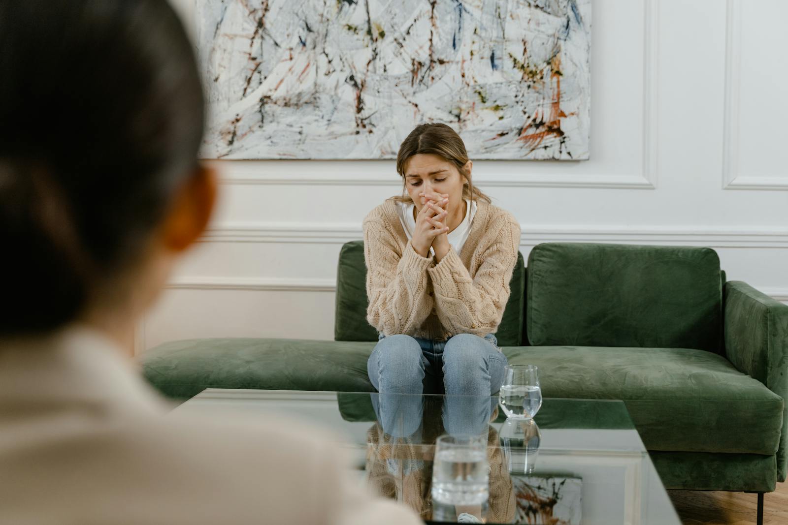 Woman in therapy session, seated on a green couch indoors, looking pensive.